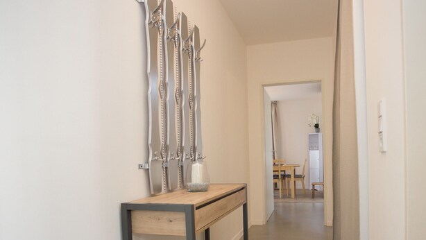 Ein Flur mit einem Holzkonsolentisch, einer Wandskulptur und einem Blick auf einen Essbereich im Hintergrund.