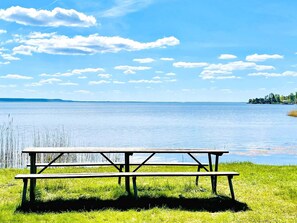 Une table de pique-nique au bord d’un lac, avec des berges verdoyantes et une rive éloignée.