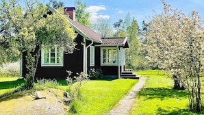 A small, dark-colored house with a red roof, surrounded by lush greenery and a clear sky. - 4 Star Holiday Home in Bralanda (Bralanda)