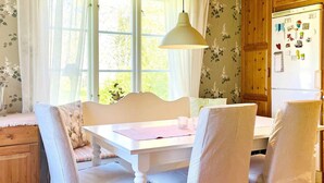 A dining area with a white table and chairs, a hanging pendant light, and a window with floral curtains. - 4 Star Holiday Home in Bralanda (Bralanda)