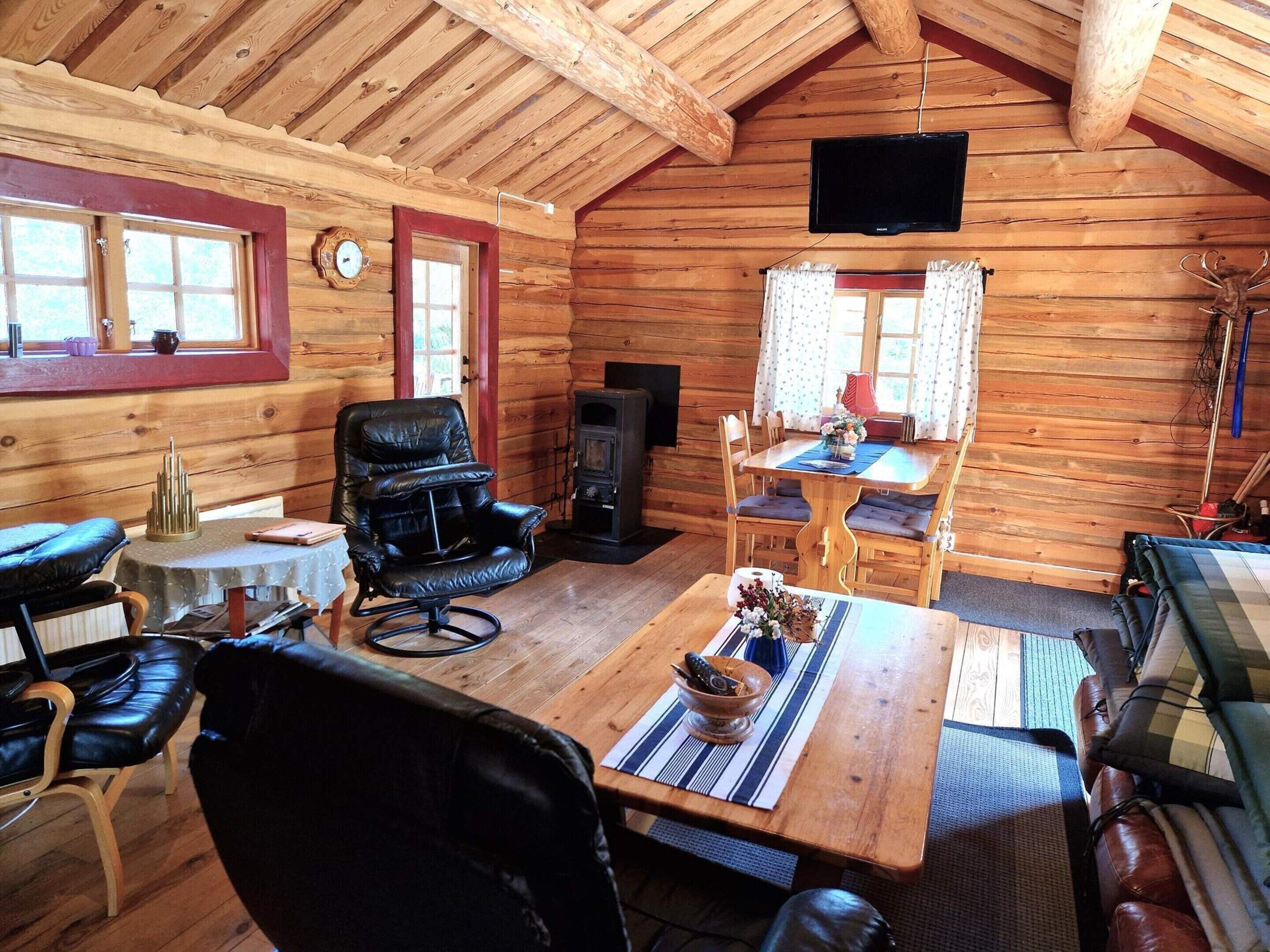 L’intérieur d’une cabane en rondins, avec une table à manger en bois, des fauteuils en cuir, une cheminée et un téléviseur fixé au plafond.