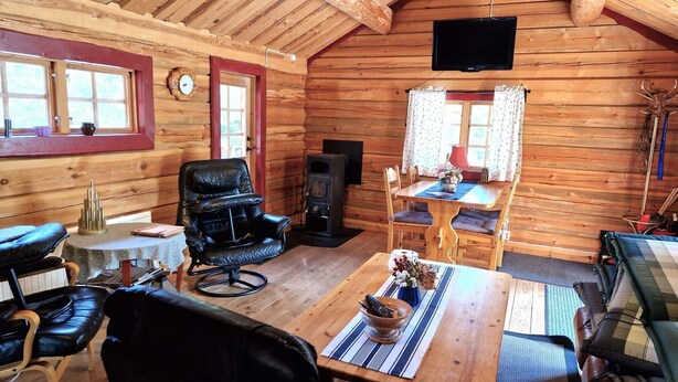 A log cabin interior with a wooden dining table, leather chairs, a fireplace, and a television mounted on the ceiling. - 7 Person Holiday Home in Saffle (Saffle)