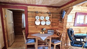A wooden interior with a dining table, chairs, a radio, and a shelf with plates.