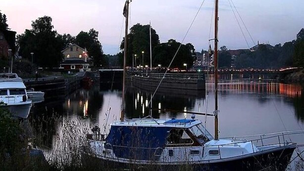 A calm river with boats docked, a lock system, and a building with lights in the background.