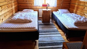 A cabin with two beds, a wooden floor, a window with curtains, and a small table.