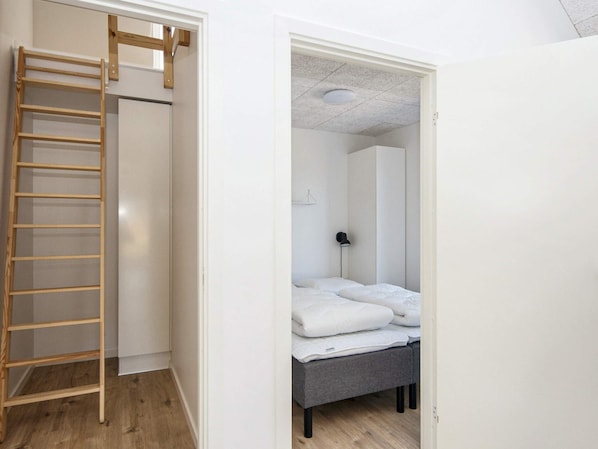 A room with a wooden ladder, a bed with white bedding, a grey bench, and a wardrobe. - 5 Star Holiday Home in Romo (Rømø)
