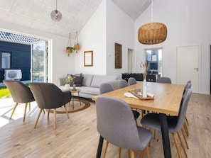 A modern living room with a wooden dining table, grey sofas, and a large window.
