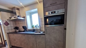 A modern kitchen with grey cabinets, a stainless steel oven, and a window above the sink. - Modernized Holiday Home With Terrace (Munstergeleen)
