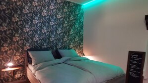 A neatly made bed with a floral-patterned headboard, a bedside table with a lamp, and a wall-mounted menu board. - Modernized Holiday Home With Terrace (Munstergeleen)