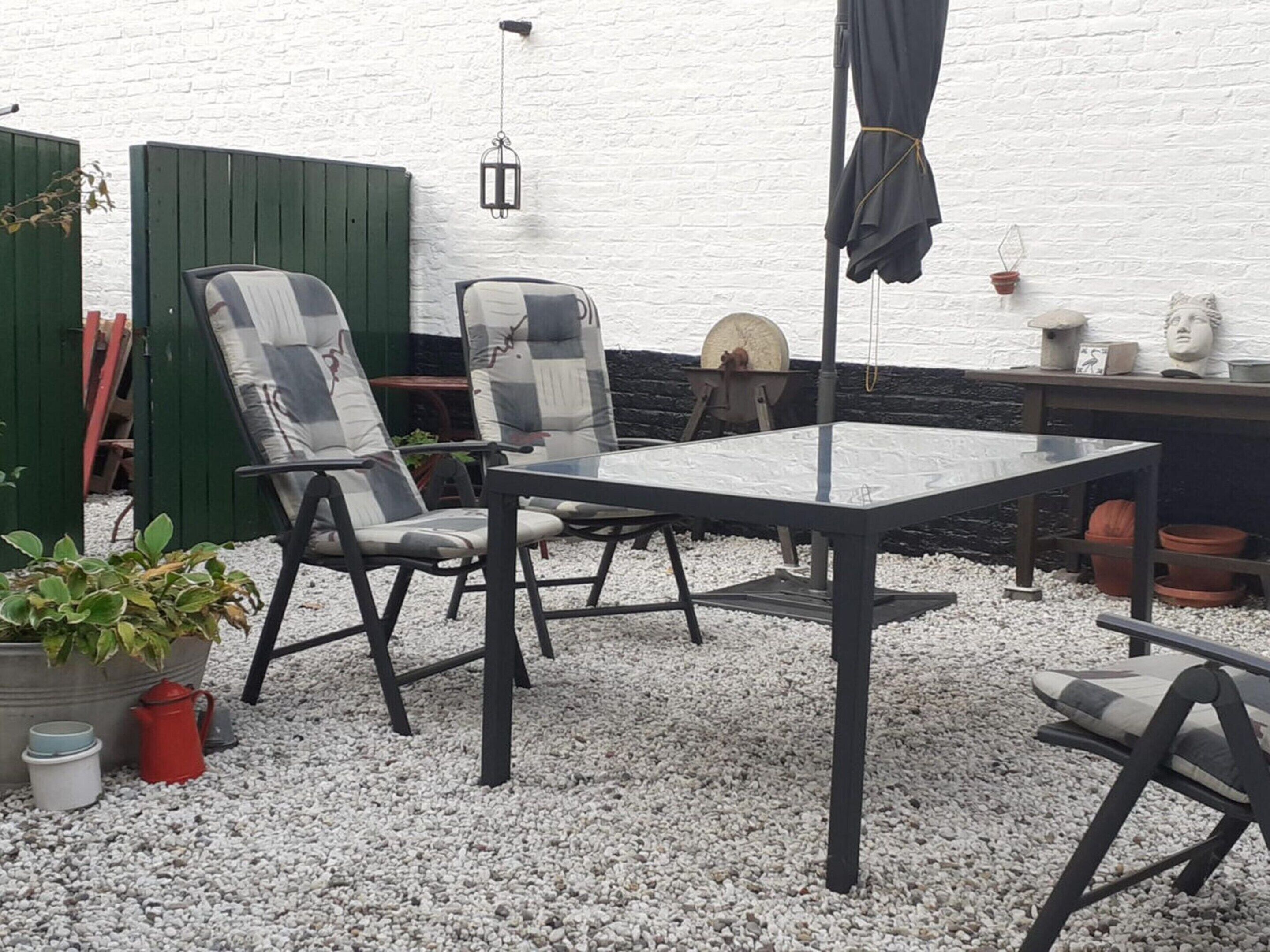 An outdoor patio with a table and chairs, a hanging lantern, and a green fence.