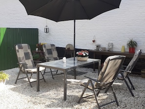 Een terras buiten met een tafel, stoelen, een zwarte parasol en een witte muur op de achtergrond.