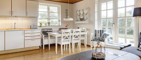 A modern kitchen with white cabinetry, a dining area with white chairs, and a large window providing natural light.