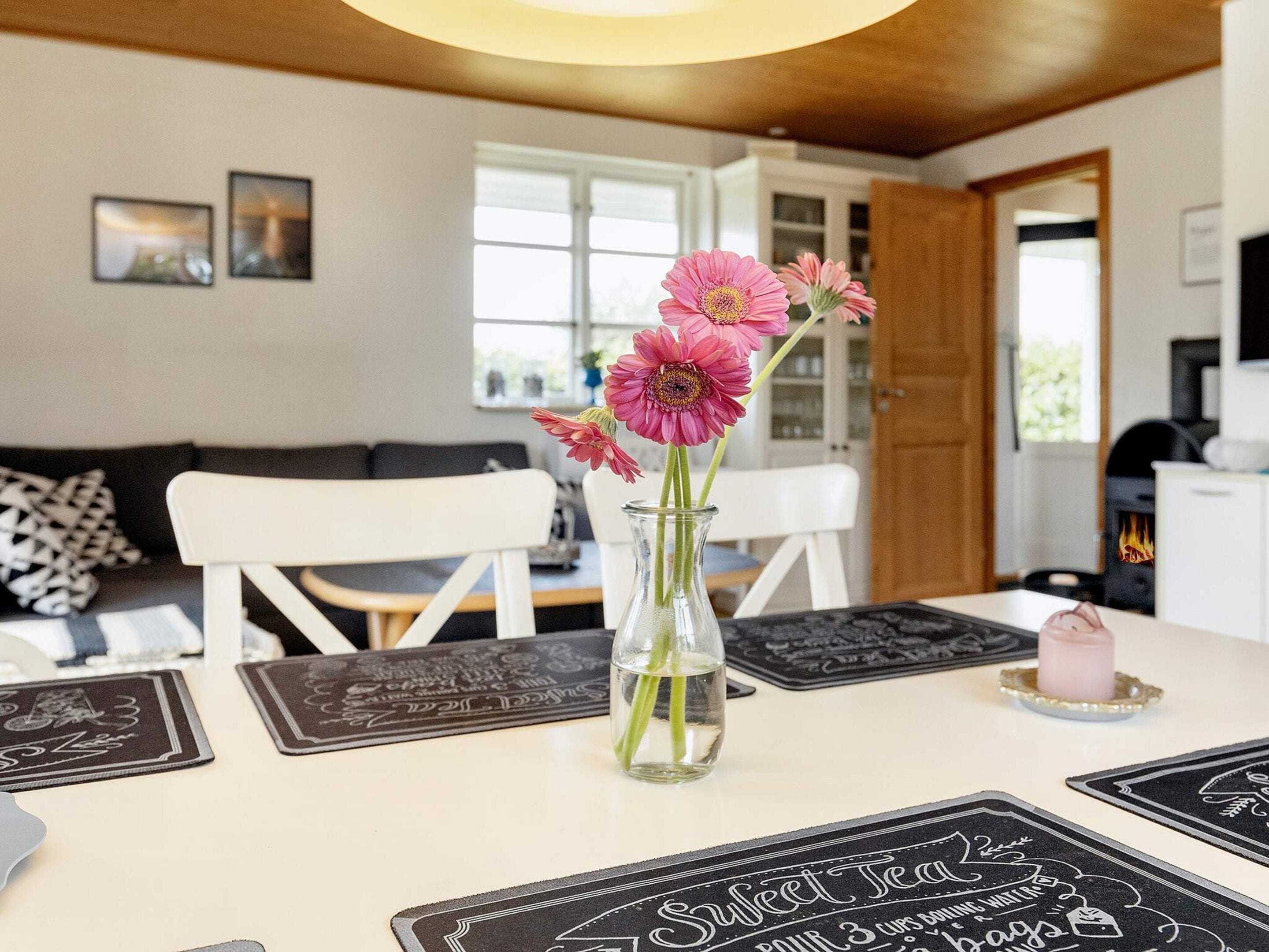 A dining table with a vase of pink flowers, black placemats with text, and a candle on the table.