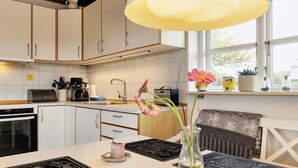Une cuisine avec des meubles blancs, une machine à café, une bouilloire et un vase à fleurs posé sur le plan de travail.