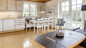 Une cuisine moderne avec des meubles blancs, un coin repas avec des chaises blanches et de grandes fenêtres qui laissent entrer la lumière naturelle.