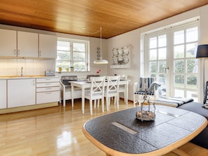 A modern kitchen with white cabinetry, a dining area with white chairs, and large windows providing natural light. - 4 Person Holiday Home in Karrebaeksminde (Karrebæksminde)