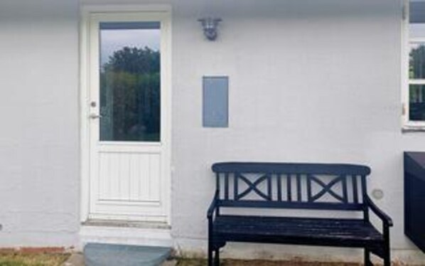 Una puerta blanca con un panel de vidrio, un banco y una pequeña placa en la pared.