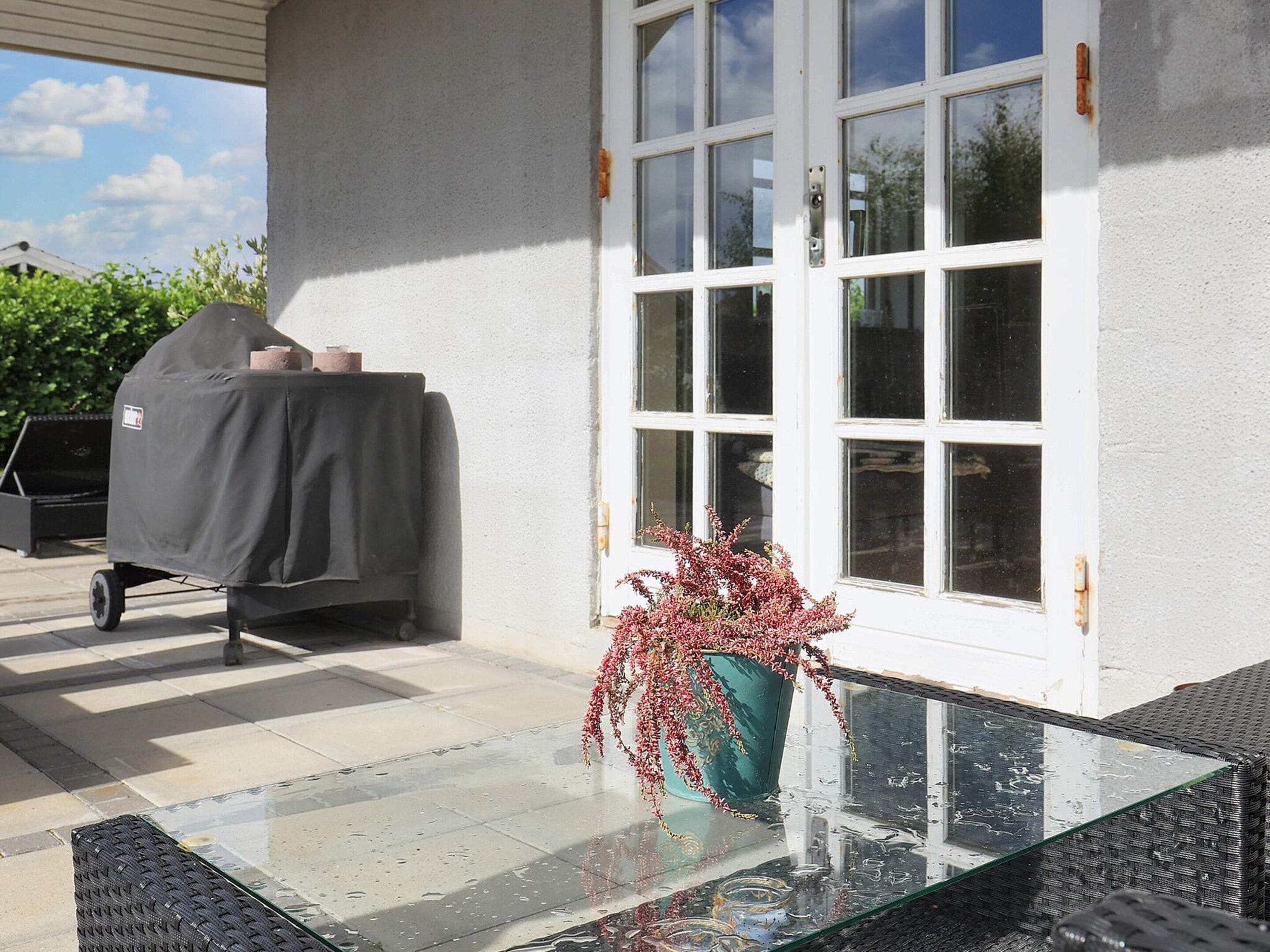 A covered grill, a glass table with a vase, and a white door with windows.