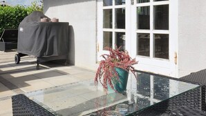 Un barbecue abrité, une table en verre avec un vase et une porte blanche avec des fenêtres.