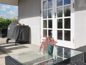 A covered grill, a glass table with a vase, and a white door with windows. - 4 Person Holiday Home in Karrebaeksminde (Karrebæksminde)