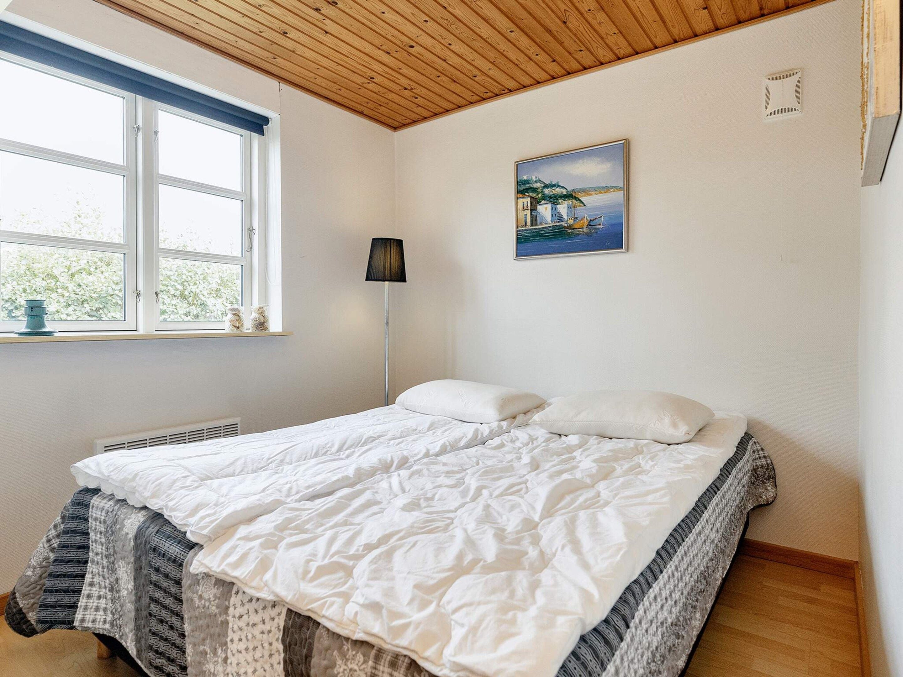 Een slaapkamer met een bed, een raam, een schilderij en een radiator.