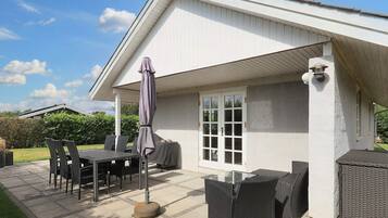 An outdoor patio with a table and chairs, a covered seating area, and a white building with a gabled roof.