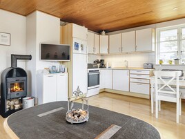 Una cocina moderna con armarios blancos, horno empotrado, estufa y comedor con mesa y sillas blancas.
