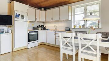 A modern kitchen with white cabinets, a built-in oven, and a dining area with white chairs and a table.