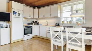 A modern kitchen with white cabinets, a built-in oven, and a dining area with white chairs and a table.
