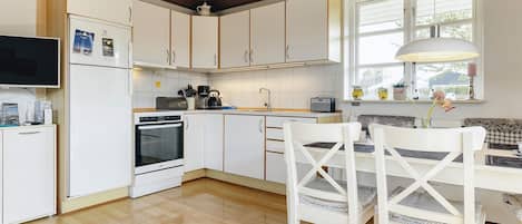 Una cocina moderna con armarios blancos, horno empotrado y comedor con sillas y mesa blancos.