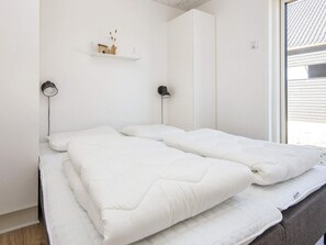 A room with a bed, two bedside lamps, a shelf with decorative items, and a window. - 5 Star Holiday Home in Romo (Rømø)