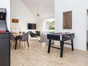A modern living room with a foosball table, a gaming console, and a dining area with chairs and a table. - 5 Star Holiday Home in Romo (Rømø)