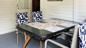 Mesa de jantar com tampo de vidro e um jogo americano floral, rodeada por cadeiras de vime com almofadas florais em azul e branco.
