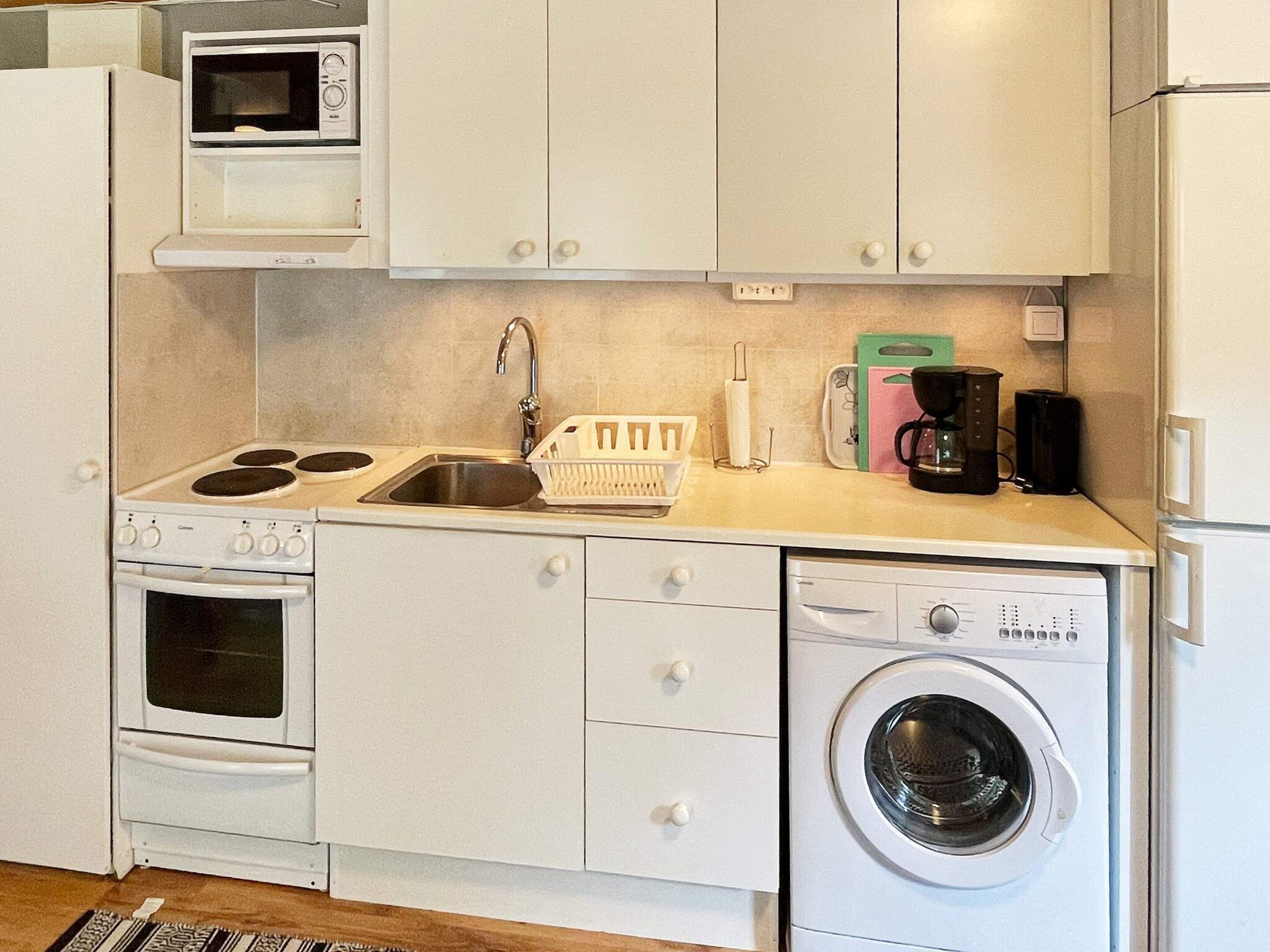A compact kitchenette with a stove, microwave, sink, and a front-loading washing machine.