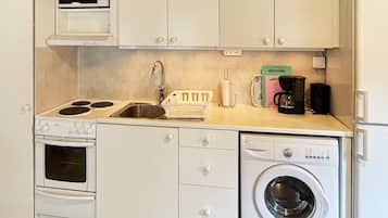 A compact kitchenette with a stove, microwave, sink, and a front-loading washing machine.