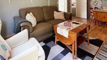 A living room with a sofa, a small table with a floral tablecloth, and a dining area with a wooden table and chairs.