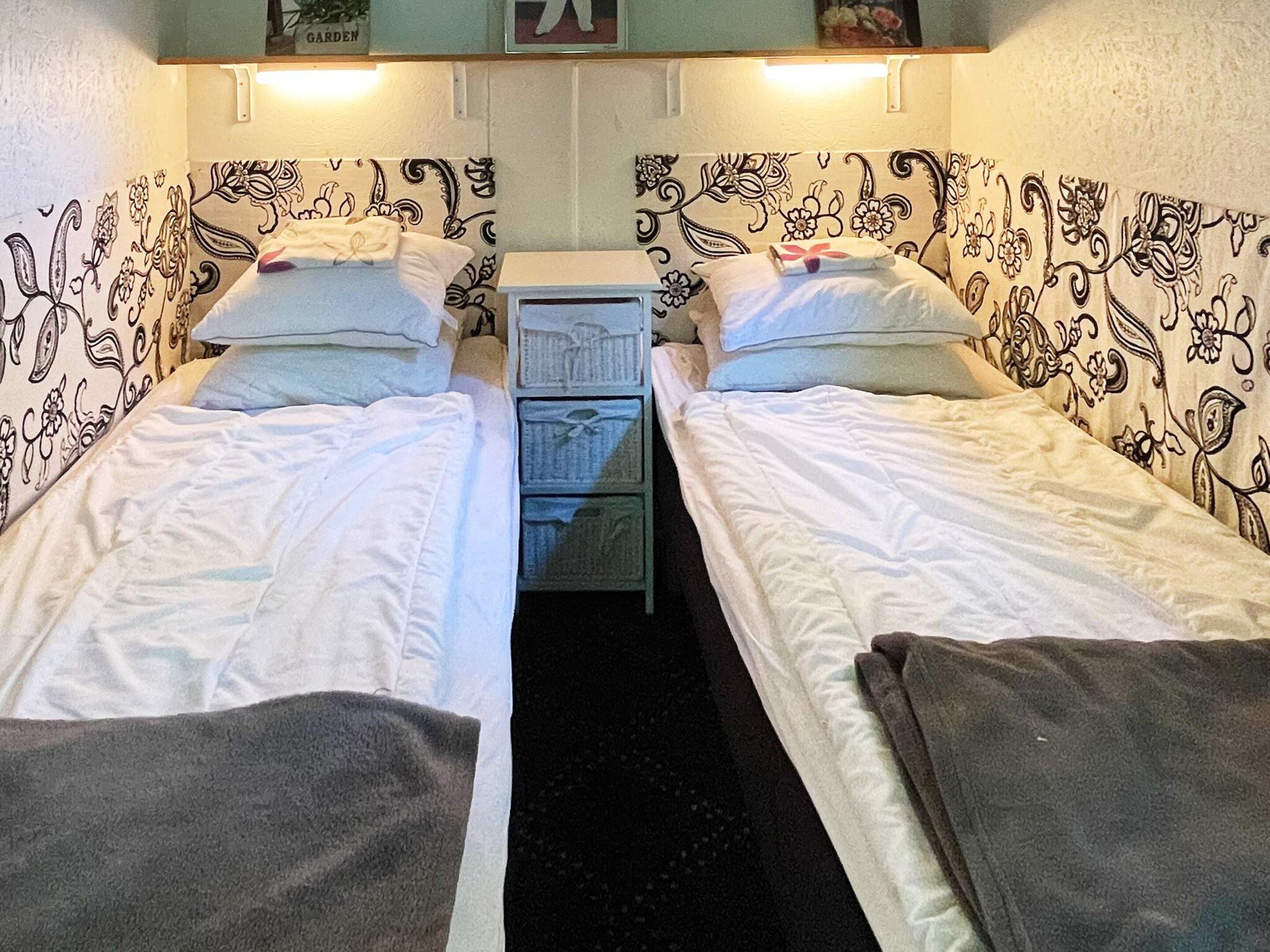 A small, narrow room with two single beds, a small dresser, and patterned wallpaper.