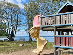 A playground with a slide and a wooden playhouse by a lake. - 4 Person Holiday Home in Morrum (Morrum)