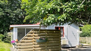 Une petite construction en bois, dotée d’une fenêtre et d’une porte, entourée d’un jardin.