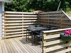 An outdoor patio with a wooden deck, a table with chairs, and a planter with flowers. - 4 Person Holiday Home in Morrum (Morrum)