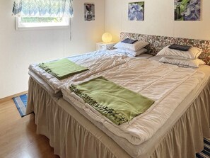 A neatly made bed with a beige bedspread and two green throw blankets, a bedside table with a lamp, and a floral-patterned headboard. - 4 Person Holiday Home in Morrum (Morrum)
