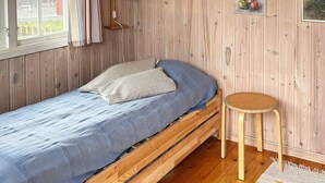A single wooden bed with a blue mattress and pillows, a small wooden stool, and a wooden wall with a window and a picture frame. - 6 Person Holiday Home in Laholm (Skummesloevsstrand)