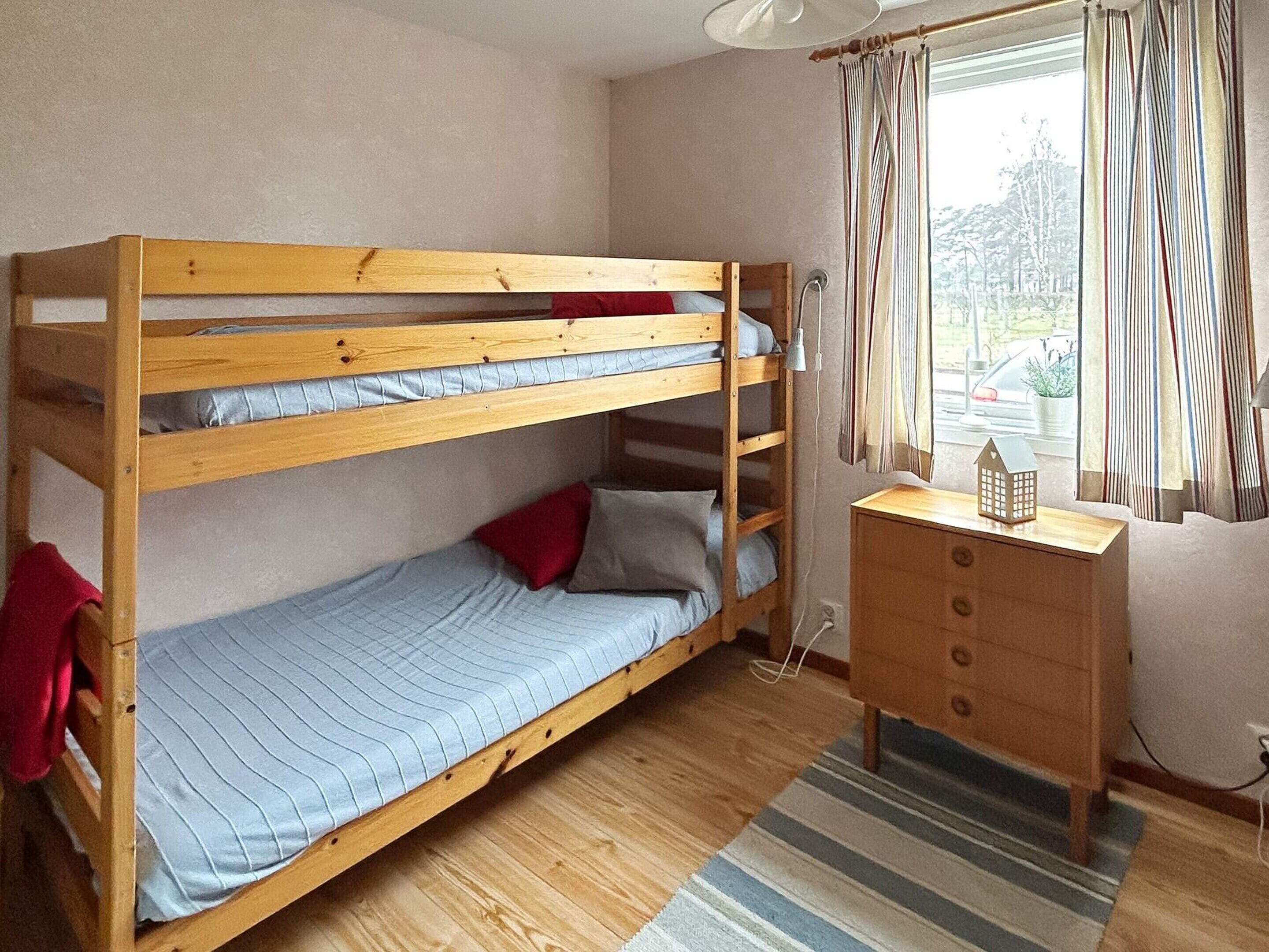 Un lit superposé avec un bureau et une lampe, une fenêtre avec des rideaux et une vue sur l’extérieur.