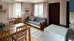 A cozy room with a sofa, a dining table with chairs, a lamp, and a refrigerator. - 6 Person Holiday Home in Laholm (Skummesloevsstrand)