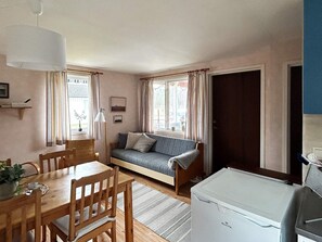 A cozy room with a sofa, a dining table with chairs, a lamp, and a refrigerator. - 6 Person Holiday Home in Laholm (Skummesloevsstrand)