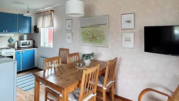 A dining area with a wooden table and chairs, a kitchen with blue cabinets, a microwave, and a stove. - 6 Person Holiday Home in Laholm (Skummesloevsstrand)