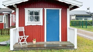 Pieni punavalkoinen mökki, jossa on sininen ovi, ikkuna ja kuisti, jossa on tuoli ja ruukussa oleva kasvi.