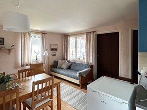 A cozy room with a wooden dining table, chairs, a sofa, and a white refrigerator. - 6 Person Holiday Home in Laholm (Skummesloevsstrand)