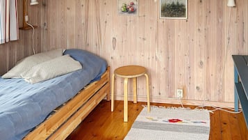 Quarto com cama de madeira, um banquinho pequeno e uma luminária na parede.