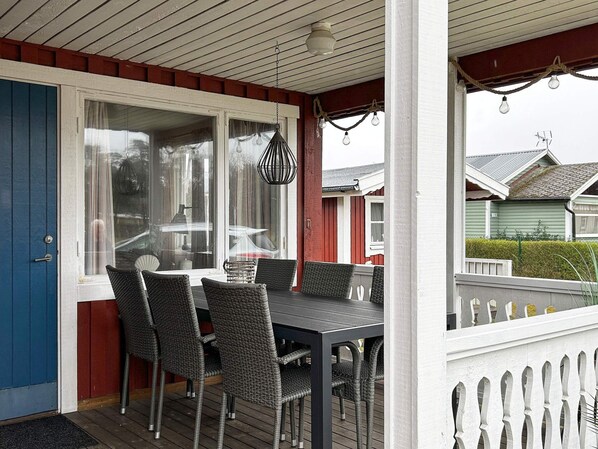 A covered outdoor seating area with a table and chairs, a white picket fence, and a view of neighboring houses. - 6 Person Holiday Home in Laholm (Skummesloevsstrand)